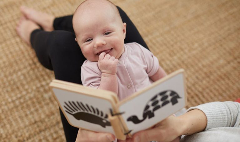 Baby laying on woman's knees looking at the Wooden Book by Lovevery