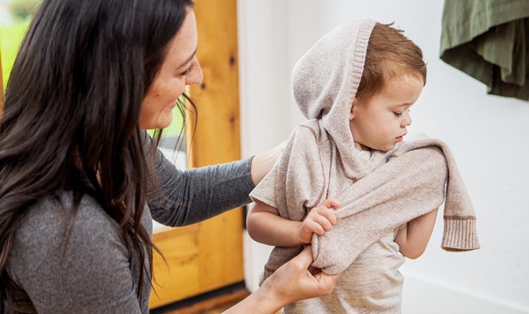 Young child putting on a sweater with help from a woman