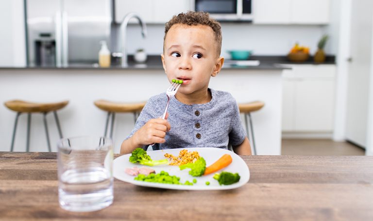 Young child eating vegetables while sitting at a table
