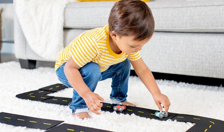Toddler pushing a toy car on a black road on carpet